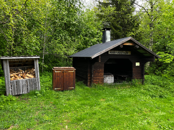 Vedförråd och soptunna bredvid stugan