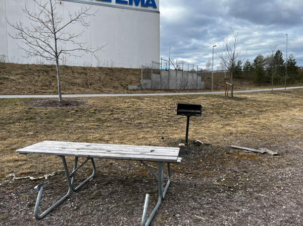 Trasigt bänkbord, grill och varuhus i bakgrunden