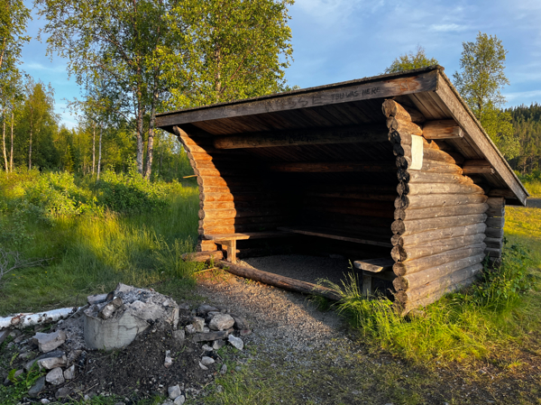 Eldstad i dåligt skick framför timrat vindskydd